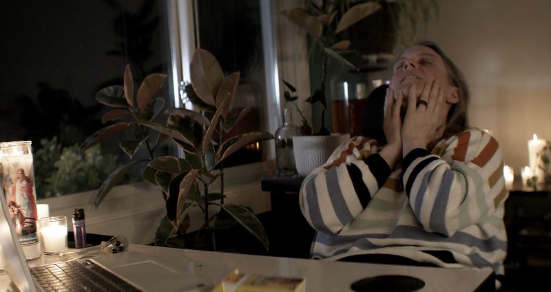 Abbey leans back by candlelight, hands on her face, smiling.